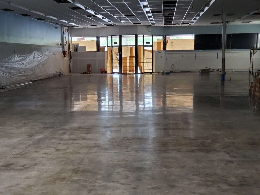 Empty room with polished concrete floor, glass doors, and exposed ceiling.