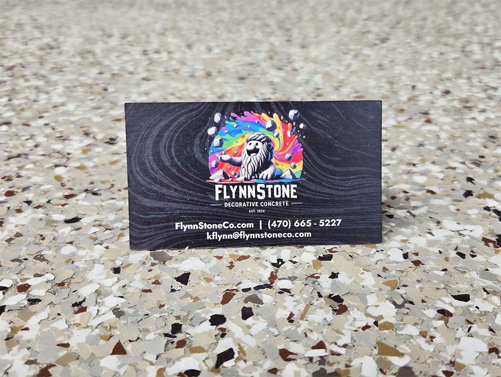 Business card on speckled surface. Card has colorful logo: man with rainbow hair, Flynn Stone logo, contact info.