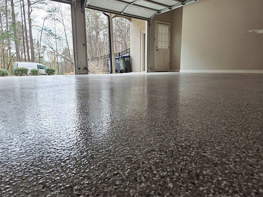 Epoxy-coated garage floor reflecting open door, trash cans, and a beige wall.