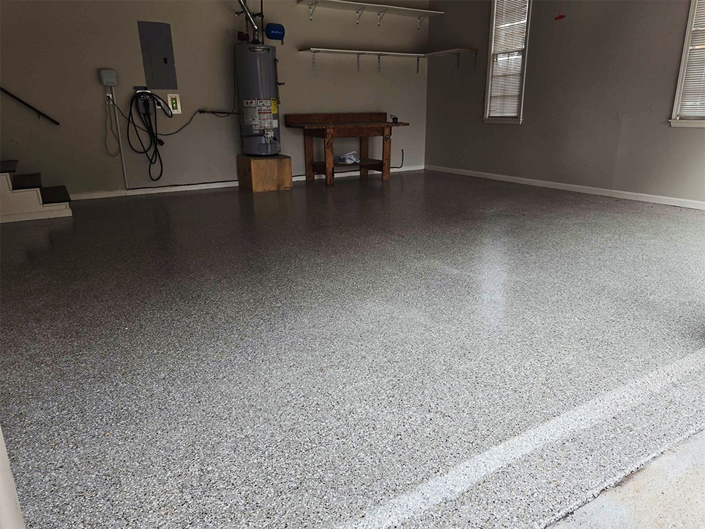 Garage with gray epoxy flooring, water heater, small workbench, and two windows.