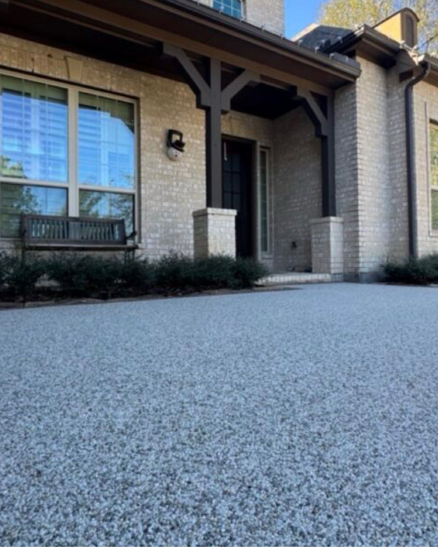 Light gray gravel driveway leads to a brick house with black door and wooden porch.
