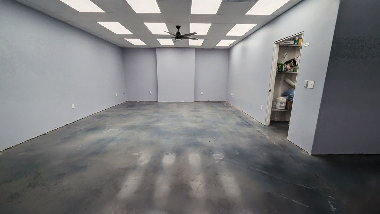 Empty room with gray walls and floor, overhead lighting, and an open doorway.