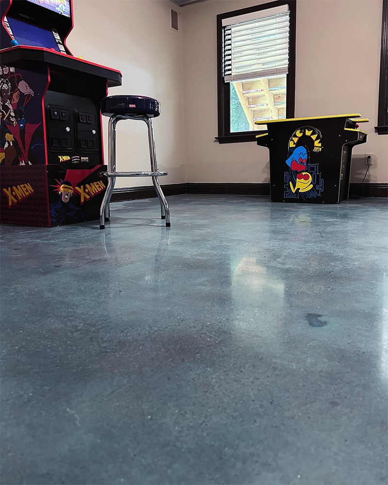 Arcade room with a blue concrete floor, arcade game, stool, and small bar.