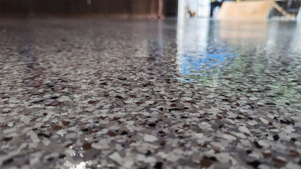 Close-up of a speckled epoxy floor with light and dark gray chips, reflecting ambient light.