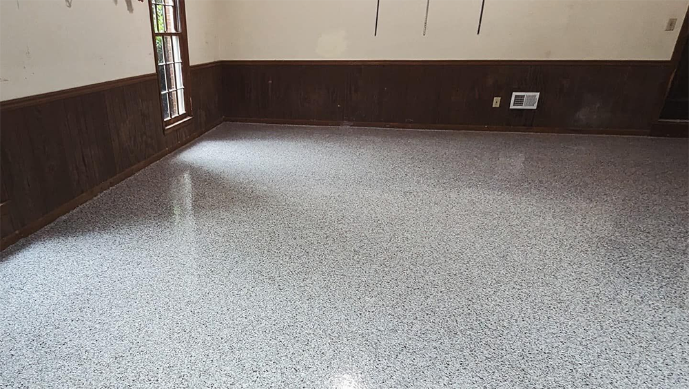 Room with gray speckled concrete floor, brown wainscoting, and a window.