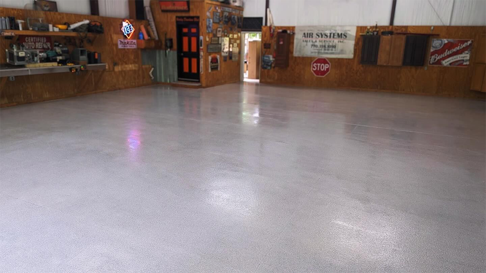 Spacious garage with a shiny, light gray concrete floor; tools, doors, and signs visible on the walls.
