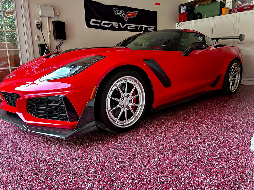 Red Corvette sports car in a garage with a Corvette banner and decorative flooring.