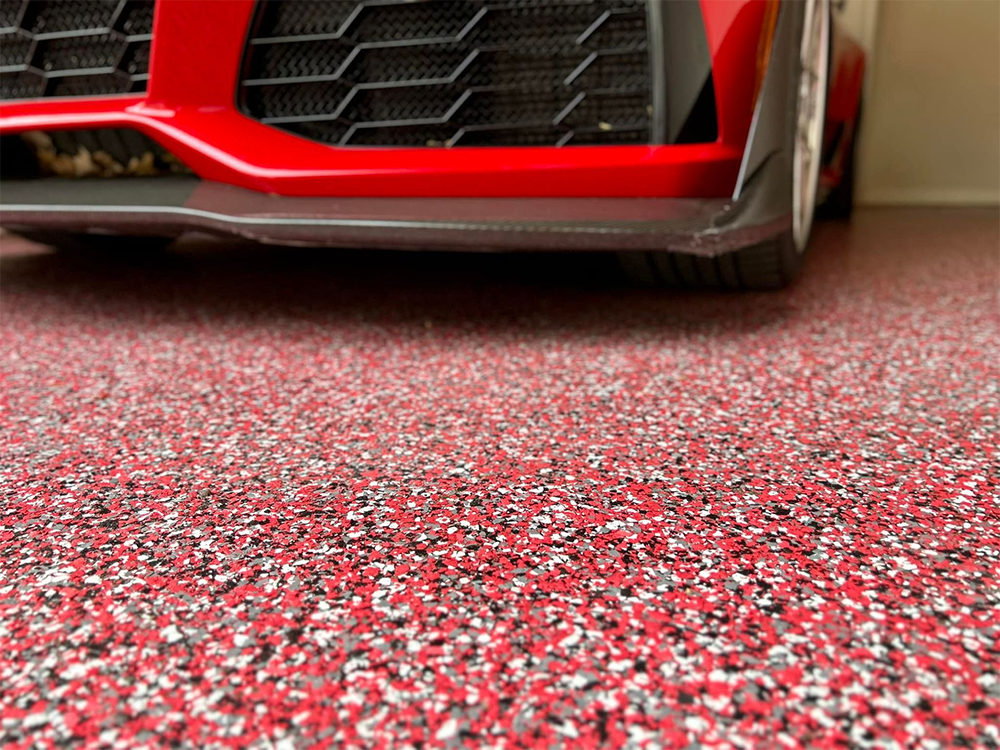 Red sports car front end over a speckled red, white, and black garage floor.