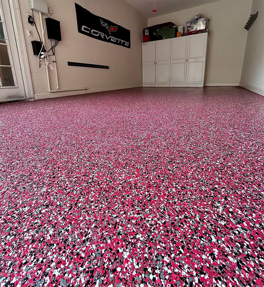 Garage with a speckled pink, white, and black floor, Corvette sign on wall, and cabinets.