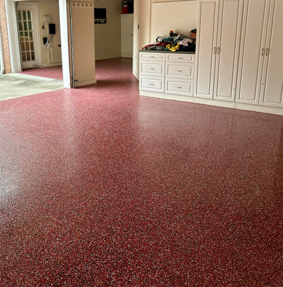 Red epoxy-coated garage floor with white storage cabinets and open doors to the outdoors.