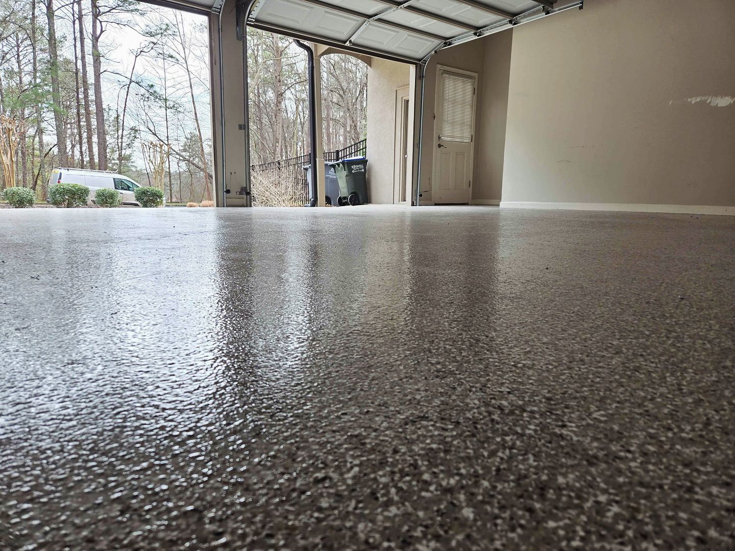 A glossy, speckled gray garage floor reflecting the open door and surrounding trees.