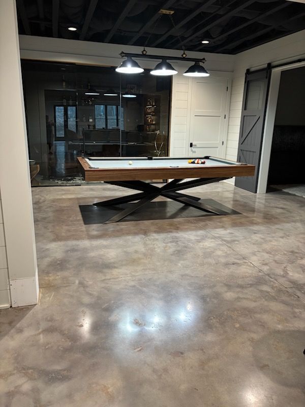 Pool table in a modern basement, with black metal base, wood trim, and overhead lighting.