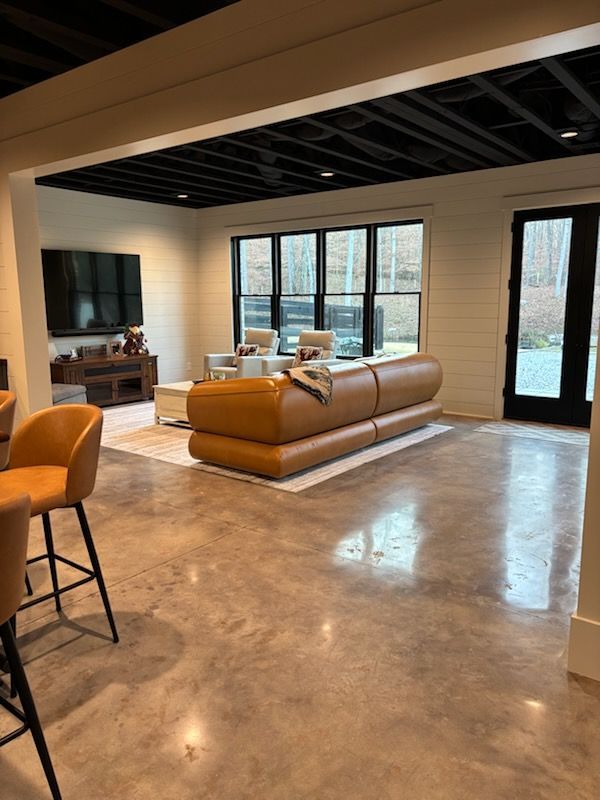 Spacious living room with tan leather sofa, black ceiling, polished concrete floor, and large windows.