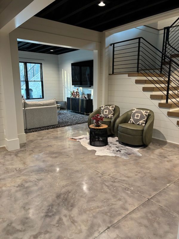 Modern finished basement with polished concrete floor, seating area, stairs, and black ceiling.