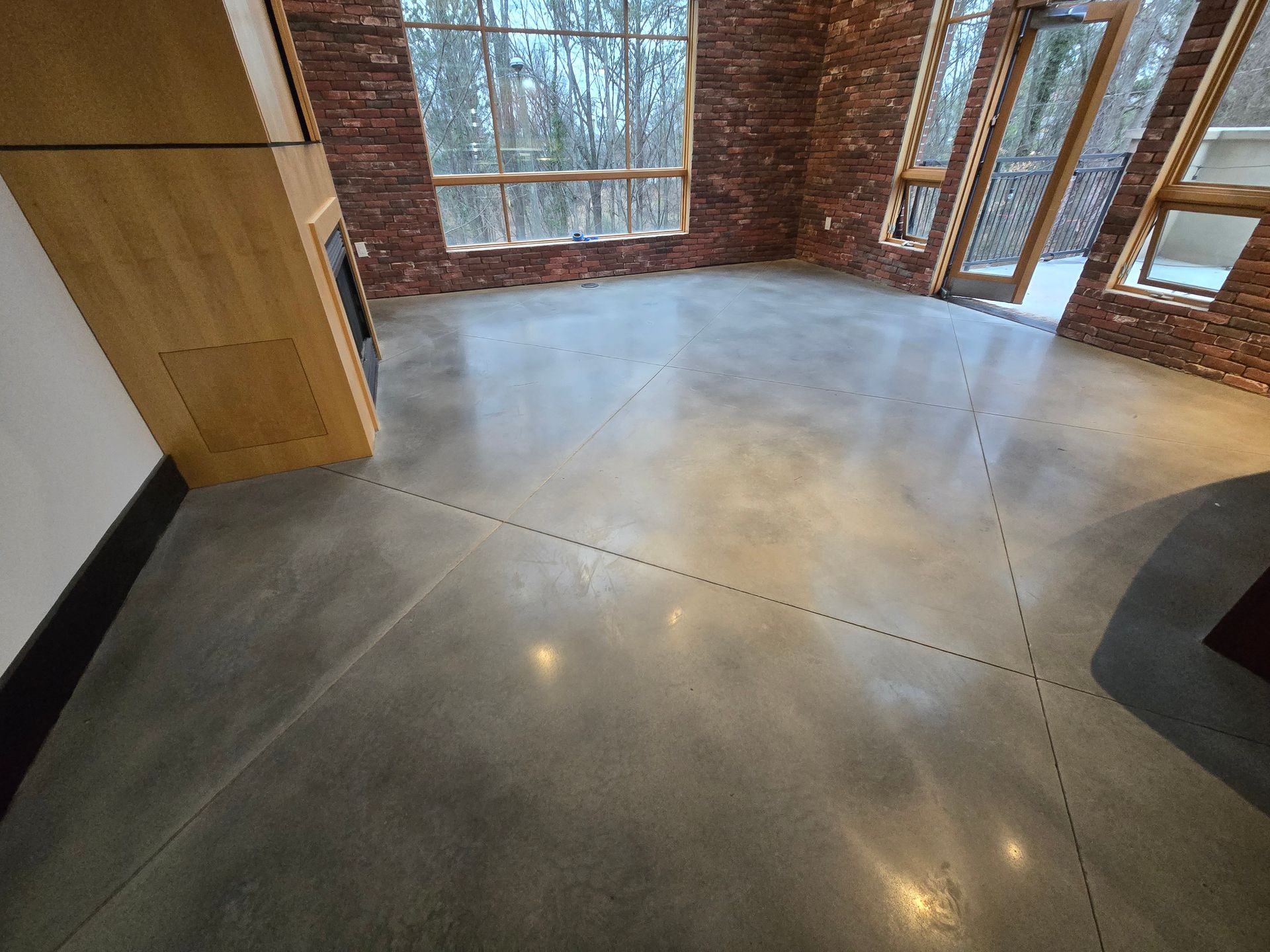 Polished concrete floor in a modern room with brick walls and large windows, reflecting light.