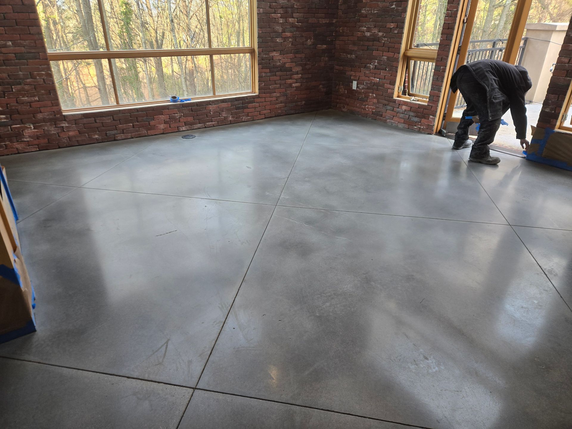 Polished concrete floor with visible lines in a room with brick walls and a person working.