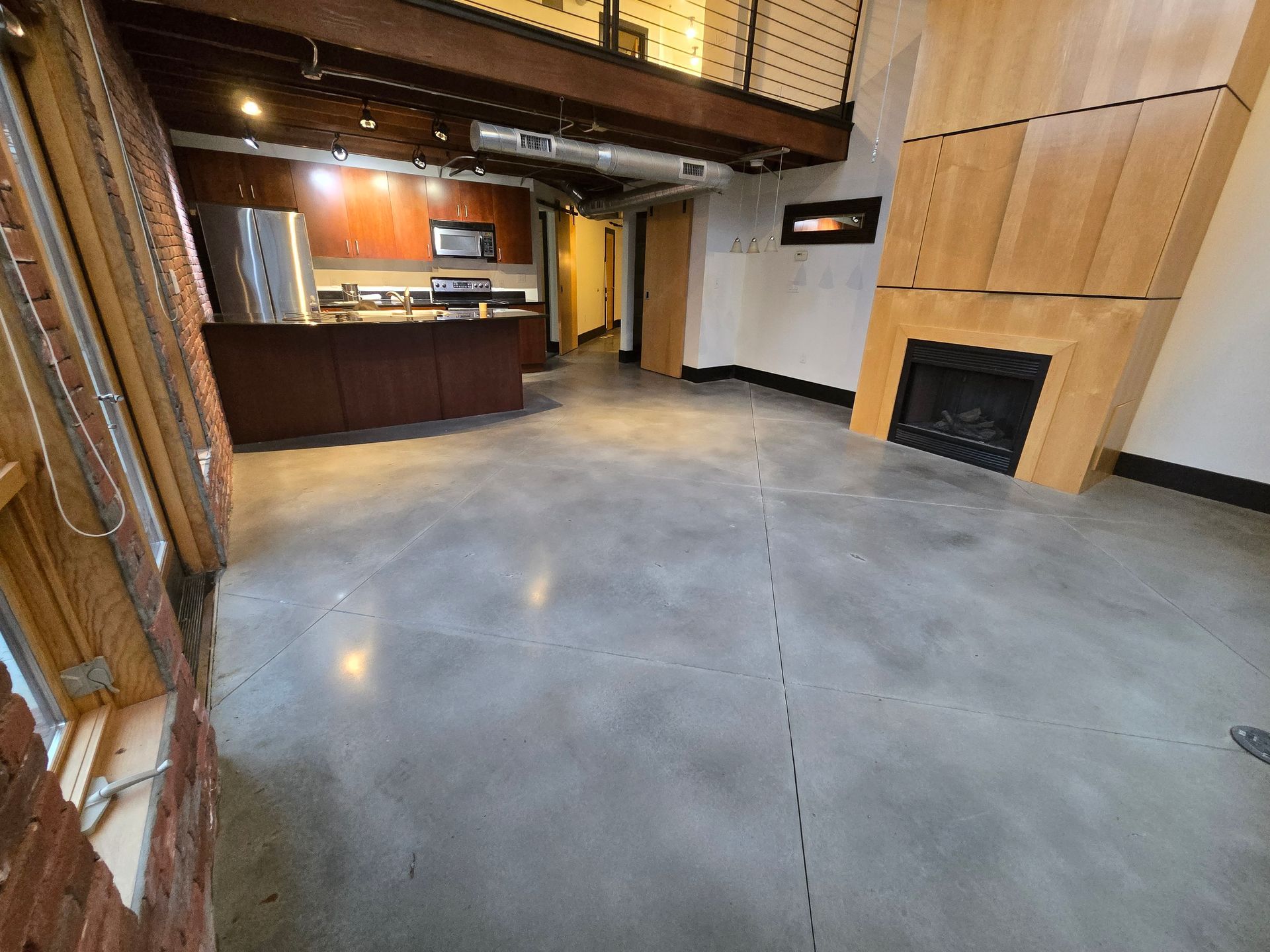 Open-concept loft with kitchen, fireplace, exposed beams, and concrete floor.