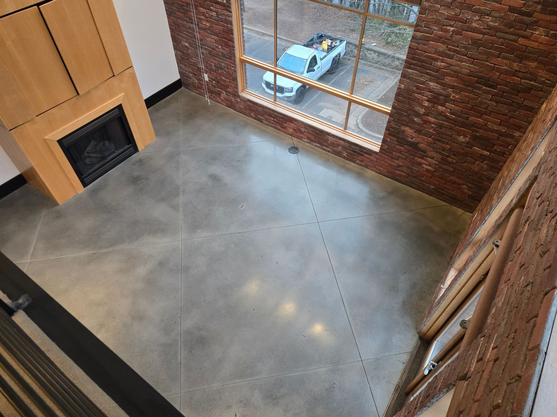 Interior shot with a concrete floor, brick walls, a fireplace, and a window overlooking a street.