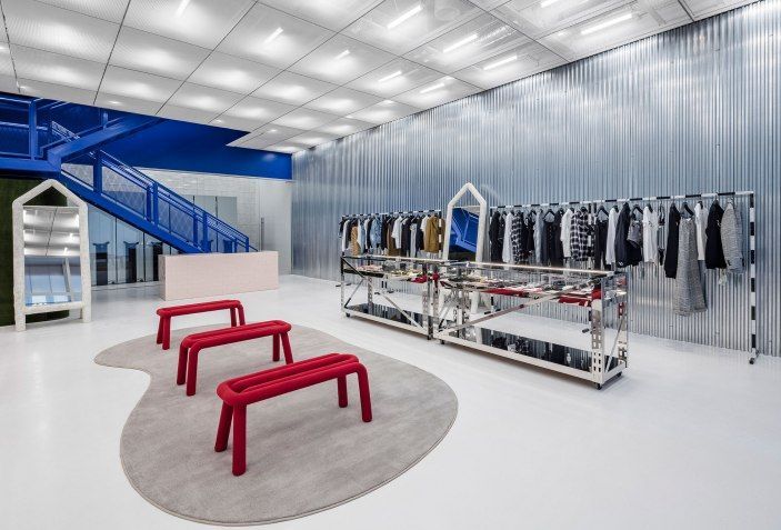Modern clothing store interior with apparel racks, red benches, and blue staircase.