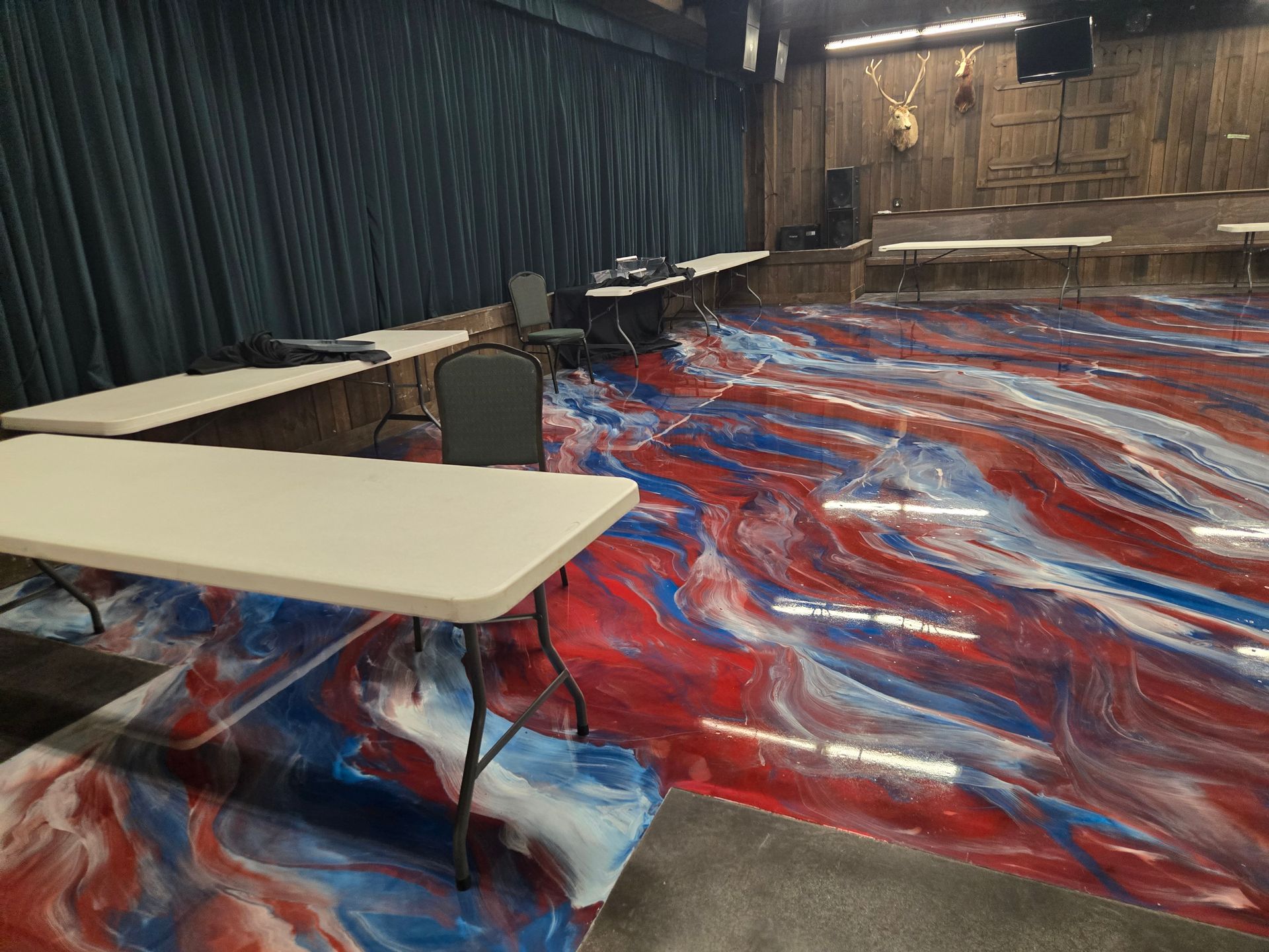 Room with red, white, and blue swirled epoxy floor, tables, black chairs, and dark blue curtains