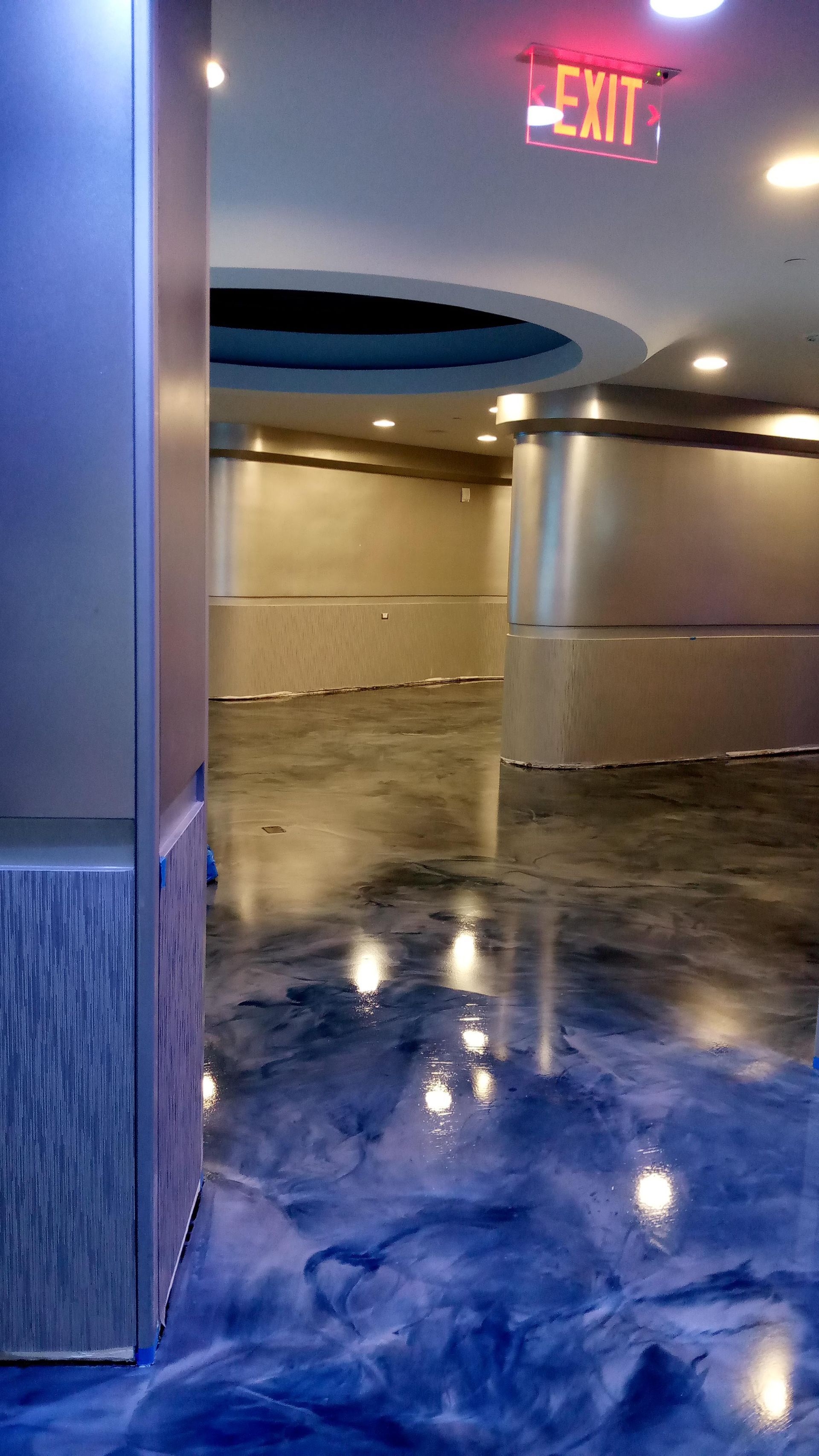 Long hallway with reflective blue floor, silver walls, and an exit sign