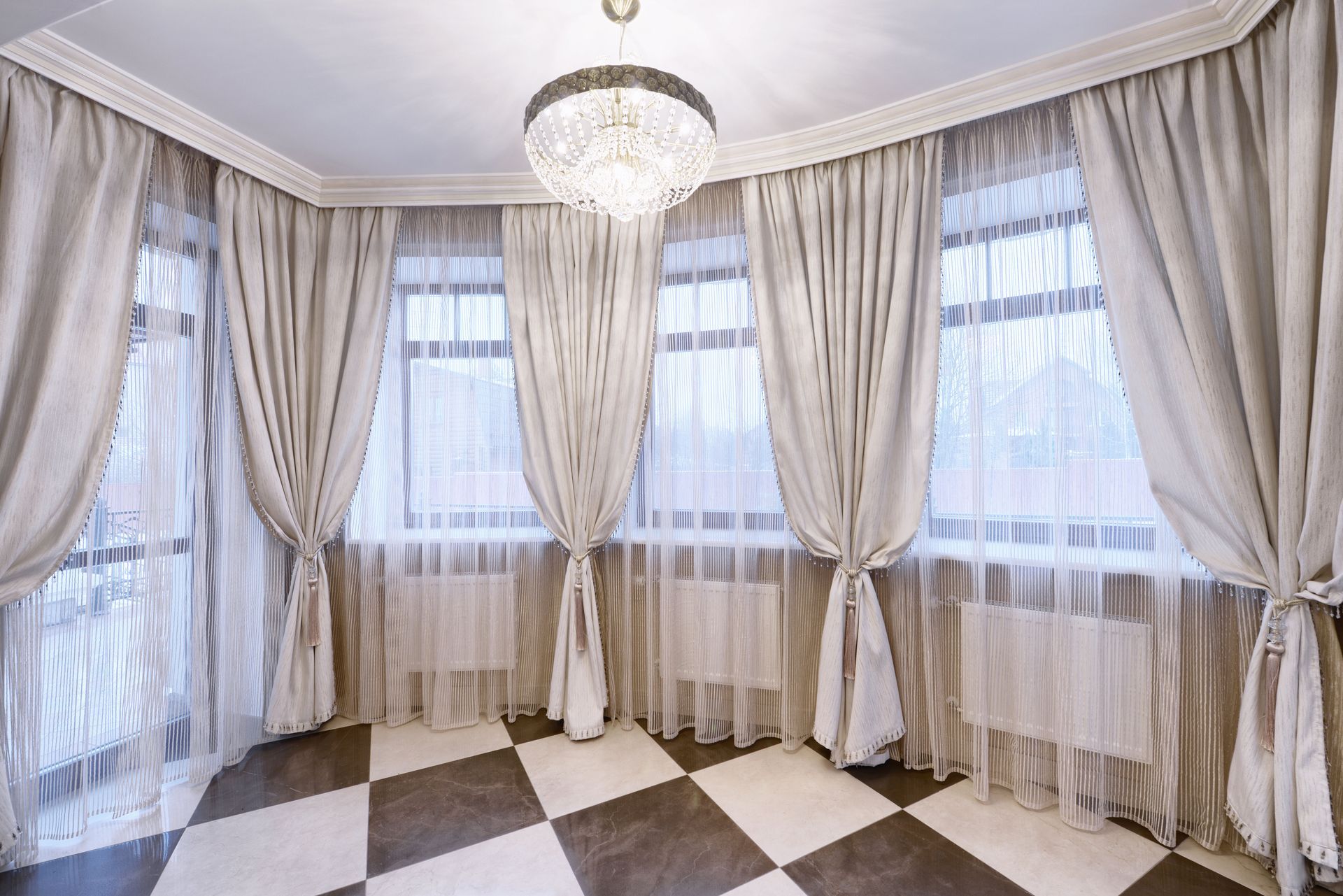 Elegant room corner with tall beige curtains, sheer drapes, chandelier, and black-and-white tiled floor