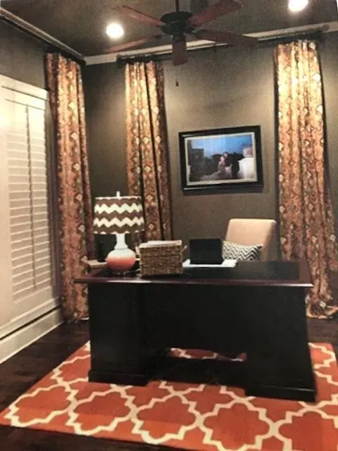 Cozy home office with desk, chair, lamp, wall art, patterned curtains, and red geometric rug.