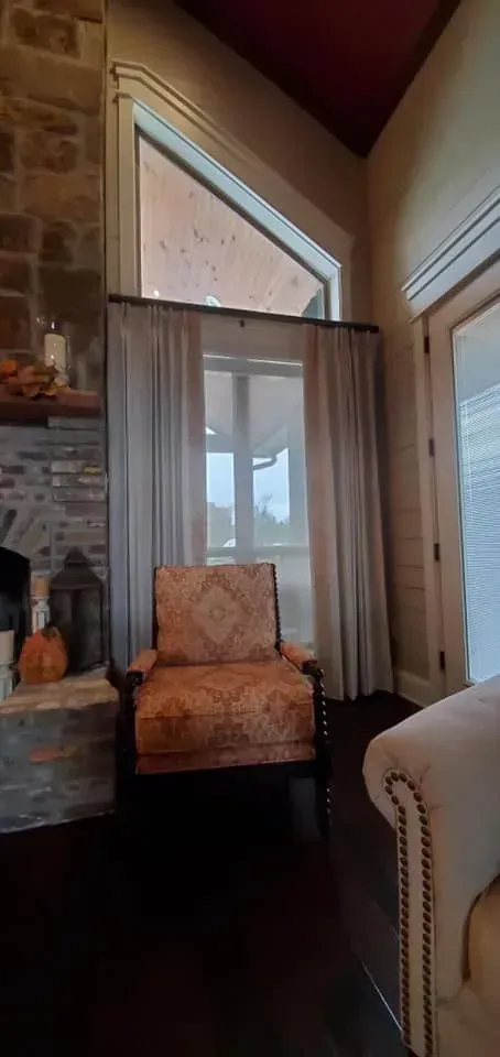 Cozy room corner with an armchair, tall window, fireplace, and sheer curtains in warm light