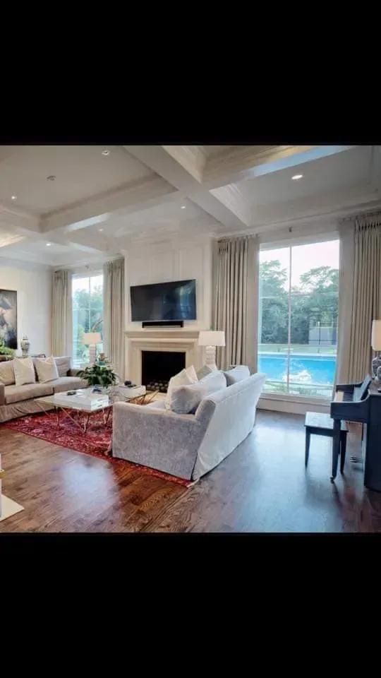 Bright living room with white sofas, fireplace, wall-mounted TV, red rug, and pool view through sliding doors