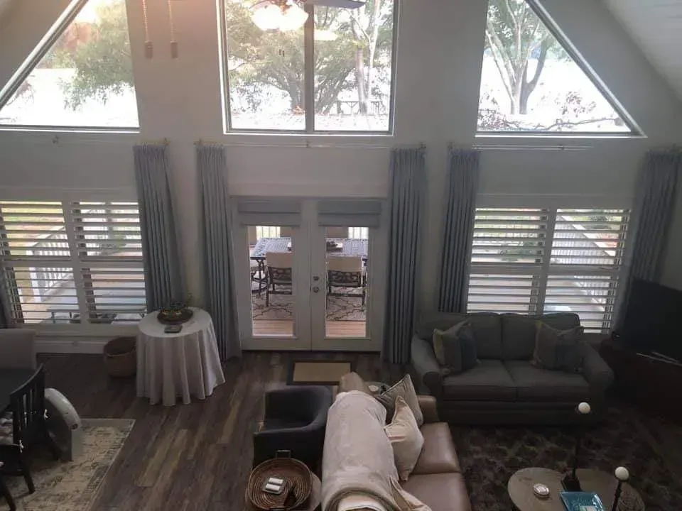 Bright living room with vaulted windows, gray sofas, wood floor, and a small round table by the curtains