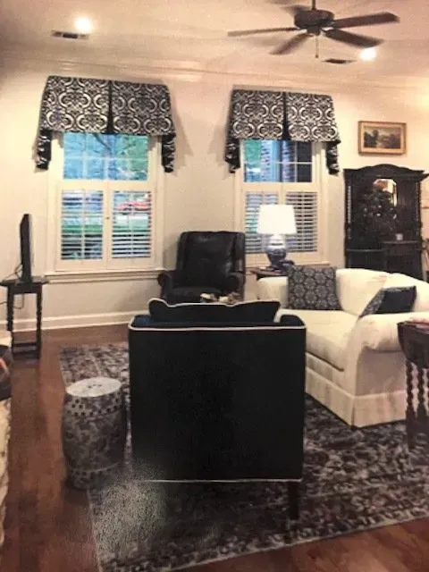 Cozy living room with white sofa, black armchairs, patterned rug, shuttered windows, and ceiling fan.