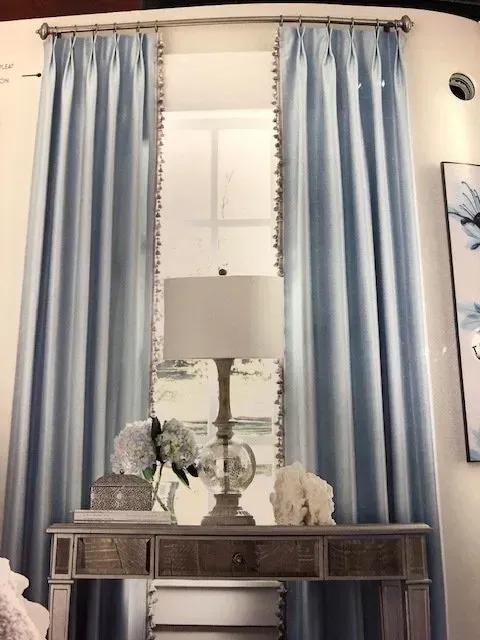Blue curtains framing a window above a mirrored console table with a lamp and decor