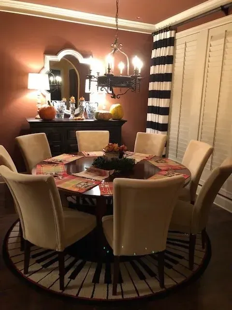 Dining room with round table, beige chairs, black chandelier, and striped curtains in warm lighting
