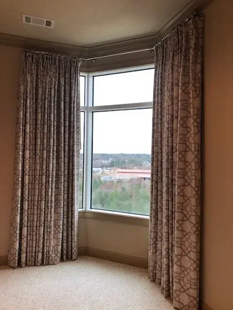 Empty room corner with bay window and patterned curtains, overlooking a distant landscape.