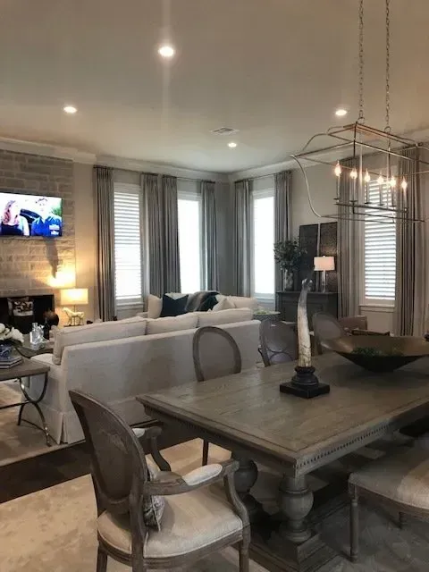 Modern open-concept living and dining room with gray decor, chandelier, and TV fireplace in the background
