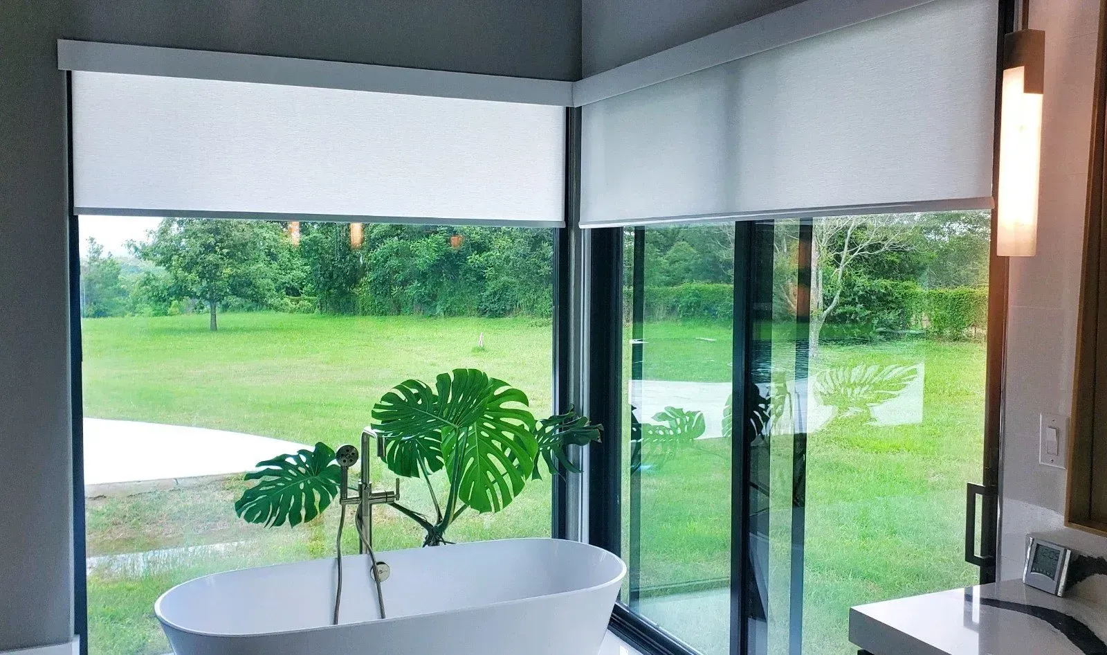 Modern interior with a round white table, potted plant, and large windows overlooking a green lawn.