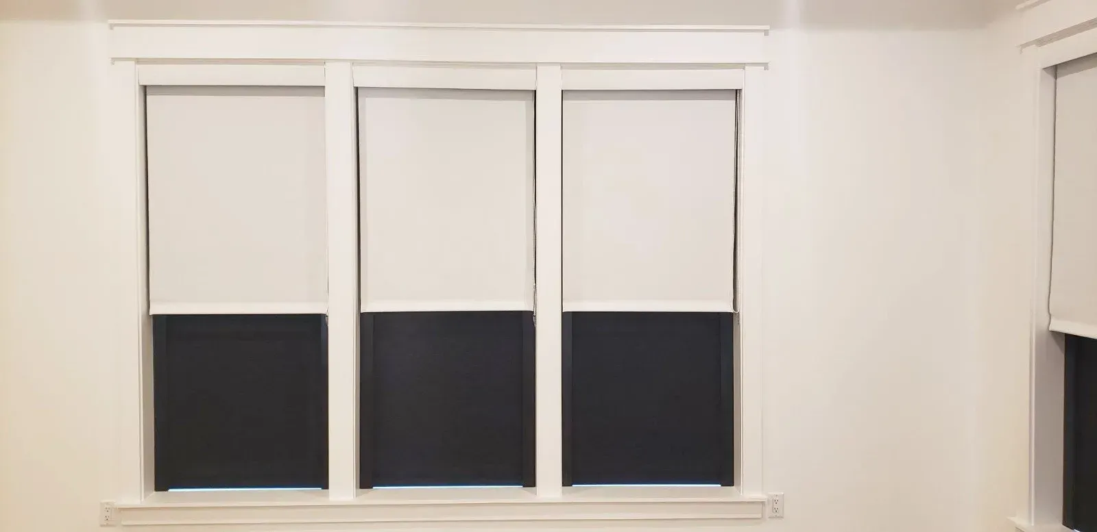 Three white windows with dark lower blinds in a white room