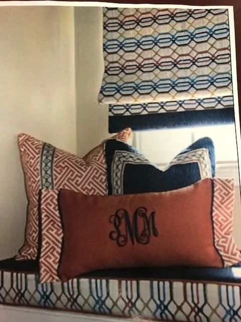 Decorative pillows on a bench by a window with a patterned Roman shade