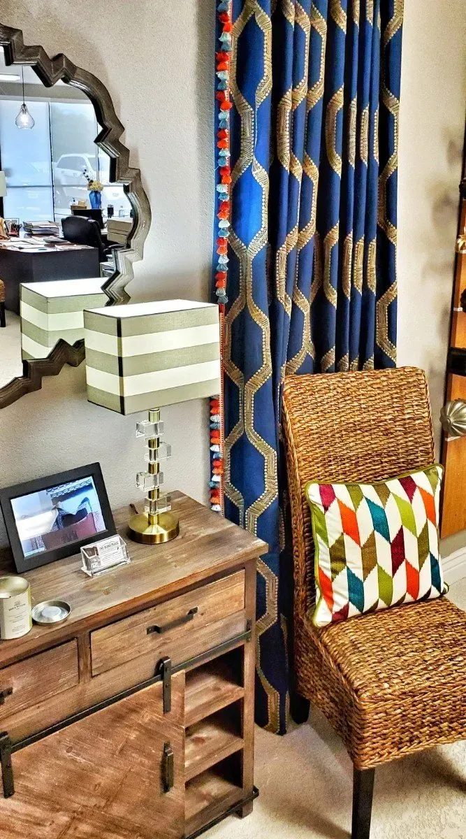 Cozy room corner with wicker chair, striped lamp, wooden side table, mirror, and blue patterned curtains.