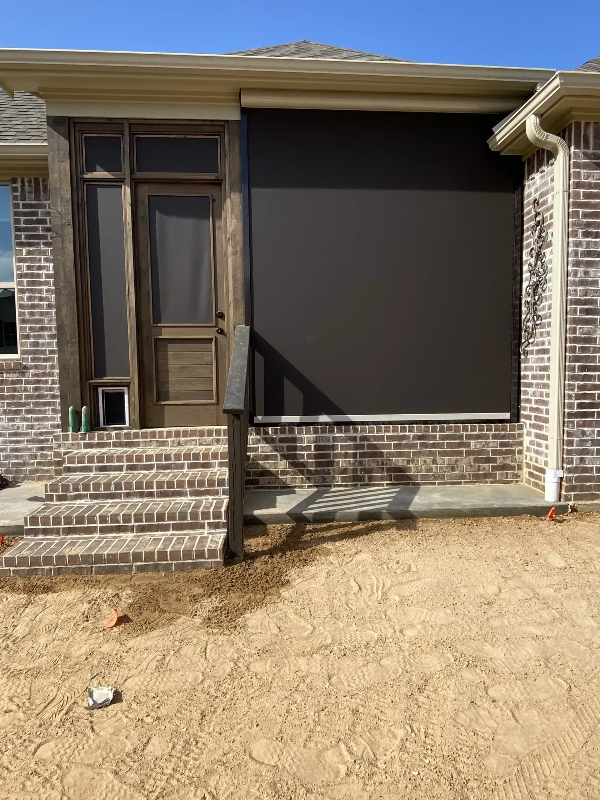 Front porch screened enclosure on a brick house with sandy yard in daylight