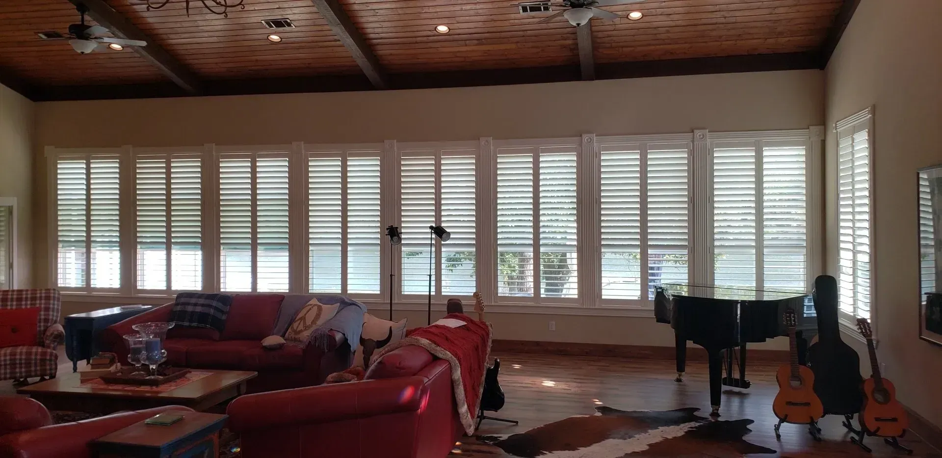 Living room with red leather sofas, white plantation shutters, and guitars by the window