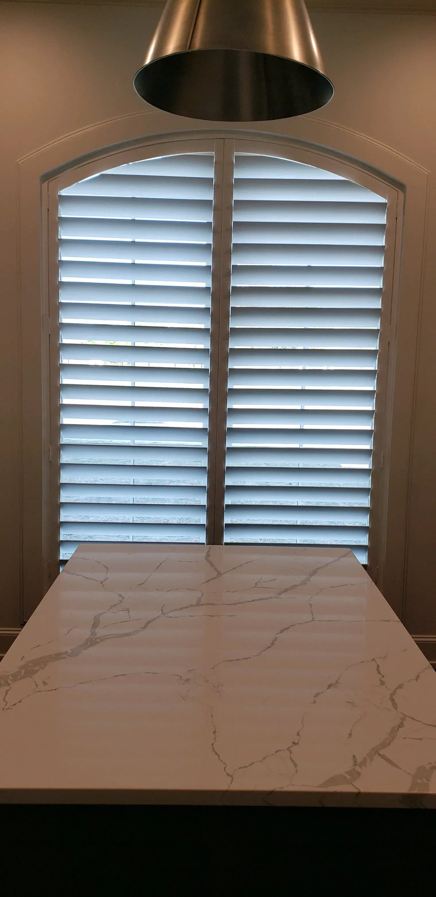 White marble table under a window with closed white shutters and a hanging light fixture.