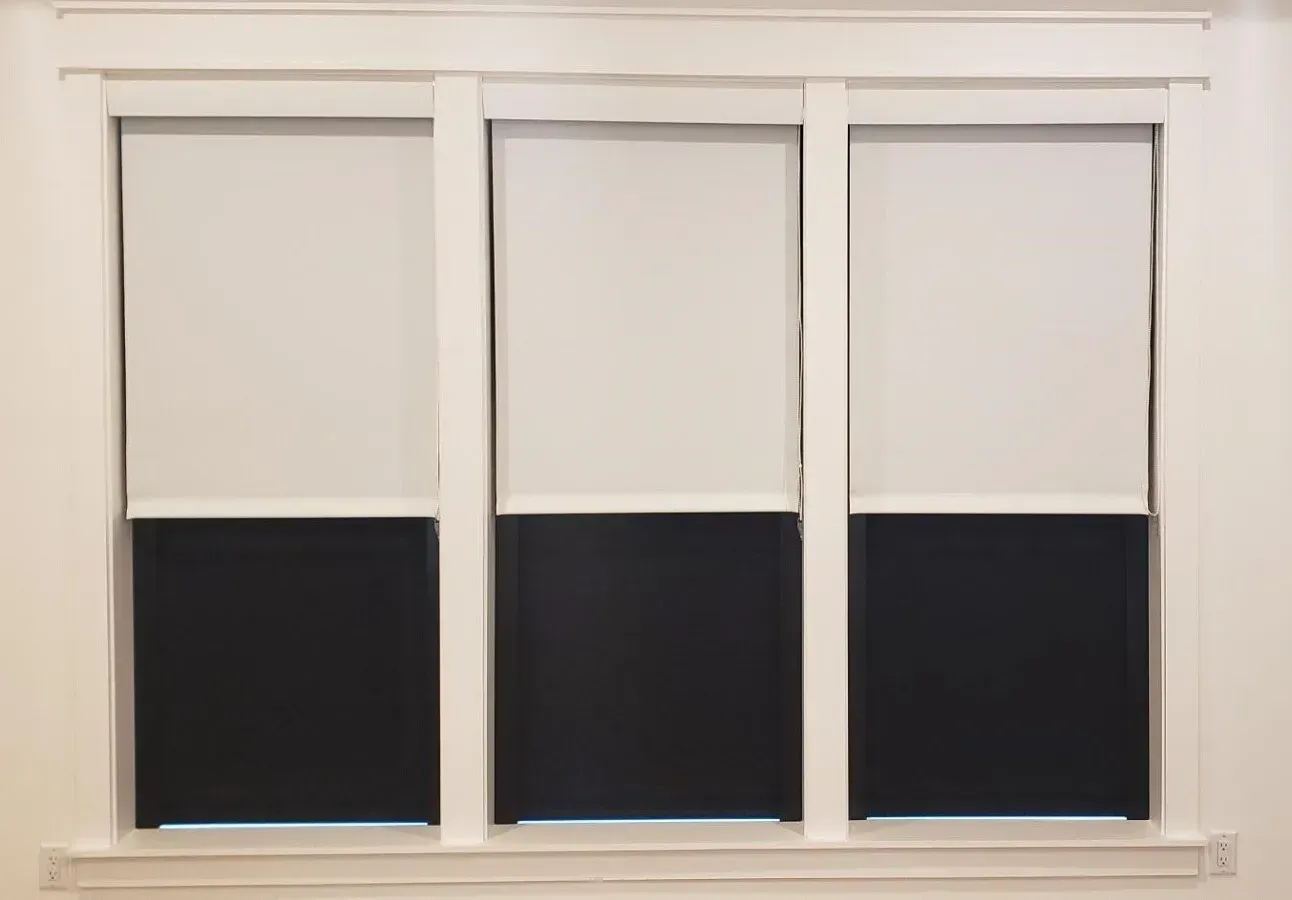 Three white window blinds partially closed, revealing dark lower sections in a white frame.
