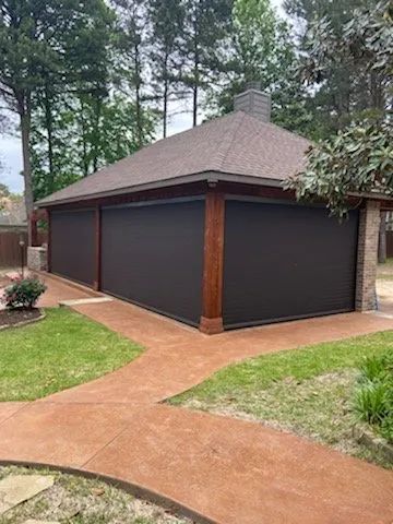Backyard garage with dark siding, brown roof, and a concrete path surrounded by trees and lawn