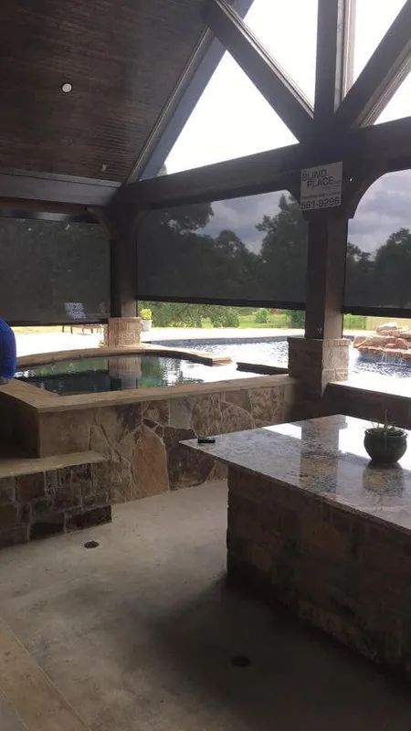 Covered outdoor pavilion with stone tables and benches overlooking a pool and landscape.