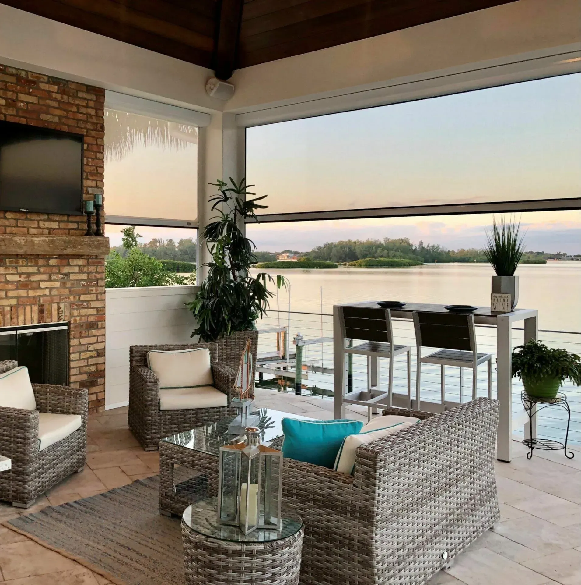 Cozy covered patio with wicker seating, glass table, and a sunset view over the water