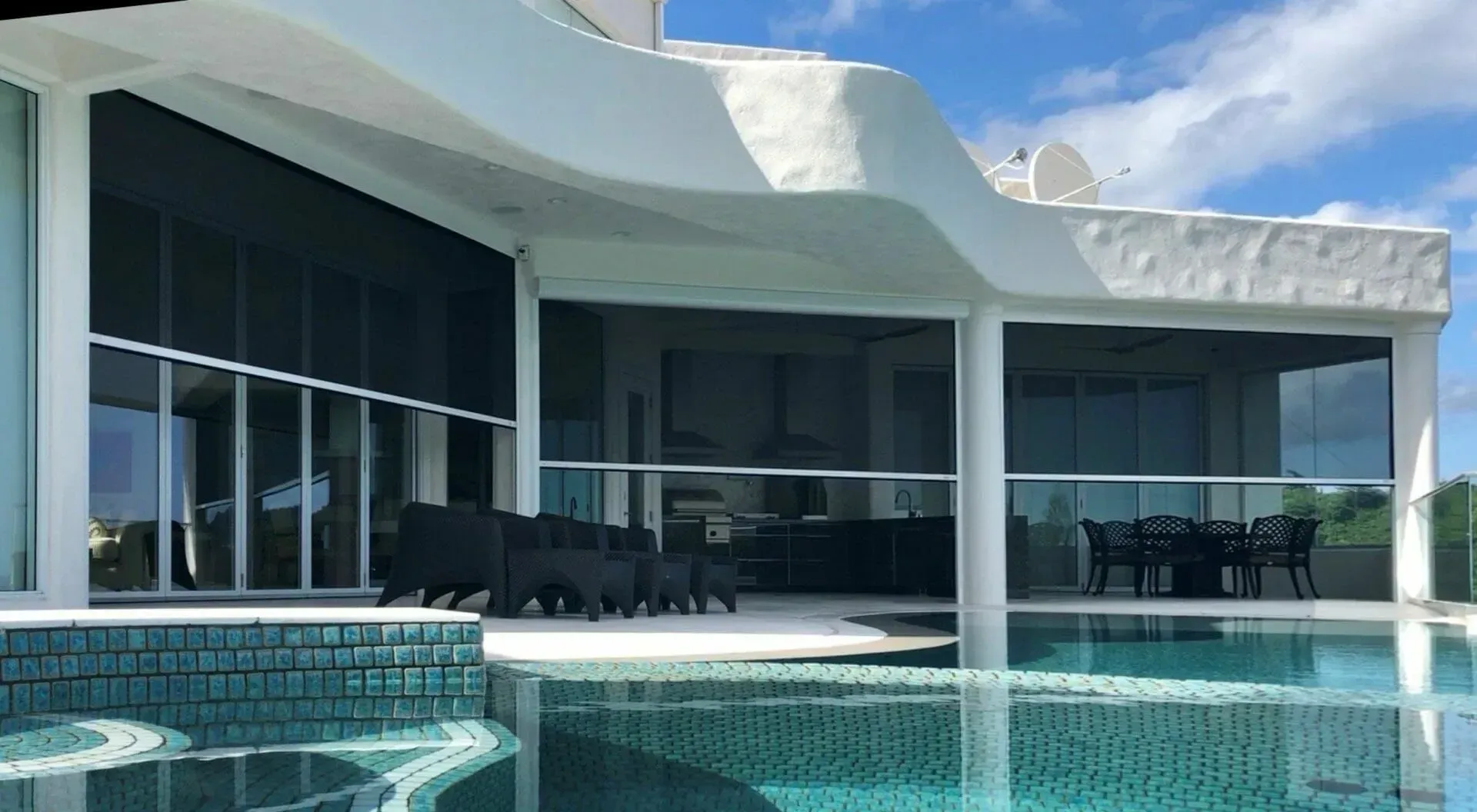 Modern luxury villa with curved pool and glass walls overlooking a bright patio