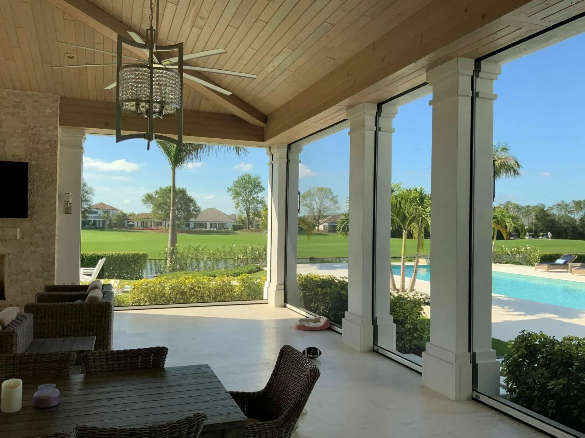 Covered patio with white columns overlooking a green lawn, pool, and palm trees on a sunny day