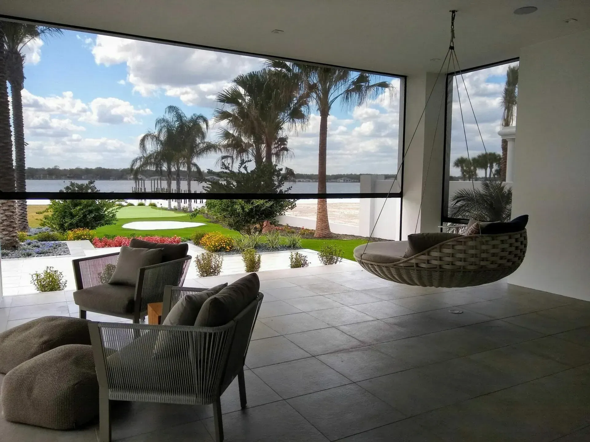 Covered patio with hanging chair, lounge seating, and oceanfront view through large open windows