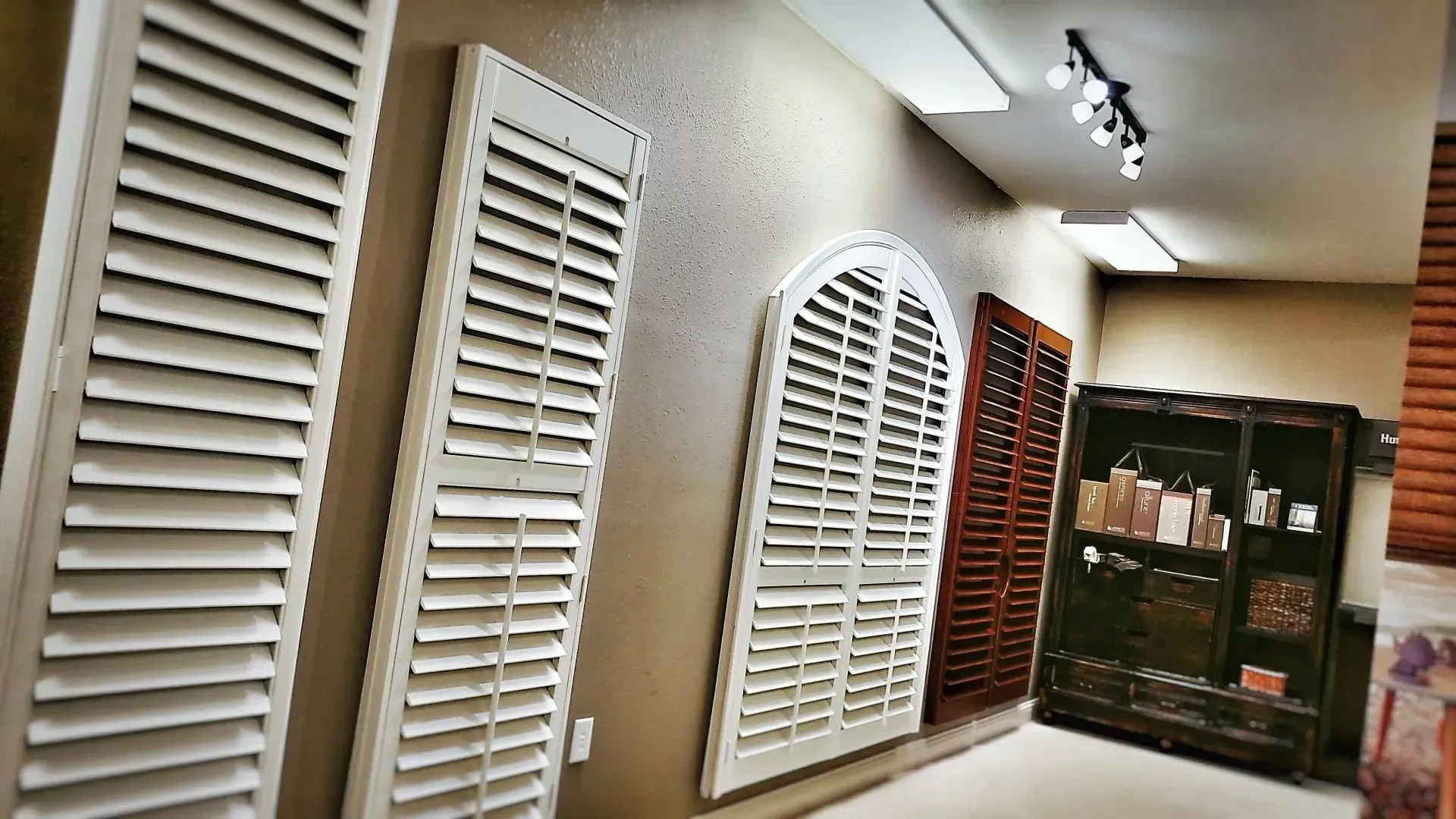 Hallway with white louvered shutters on display and a cabinet at the end